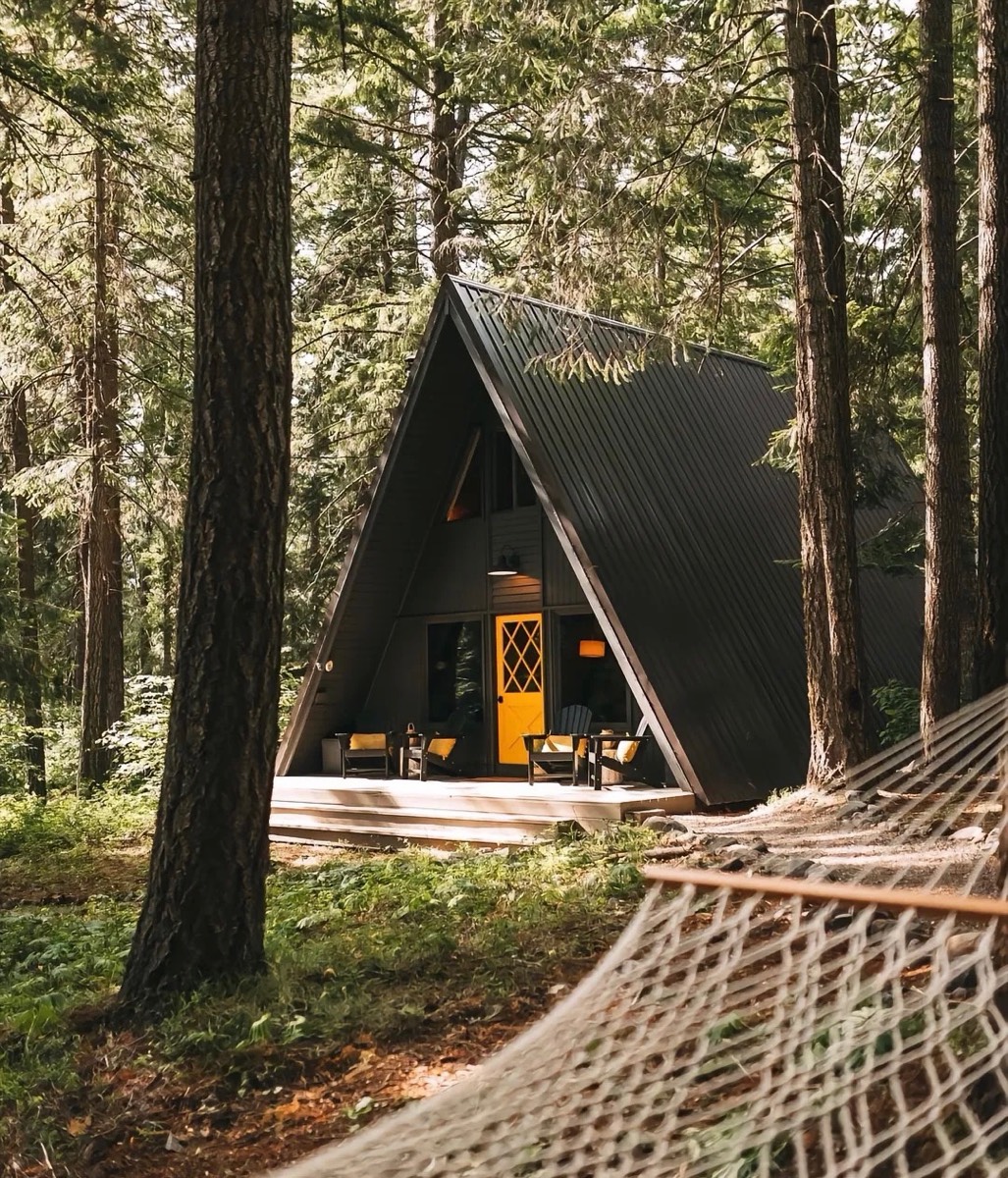 Dark A-frame cabin among tall woodland trees
