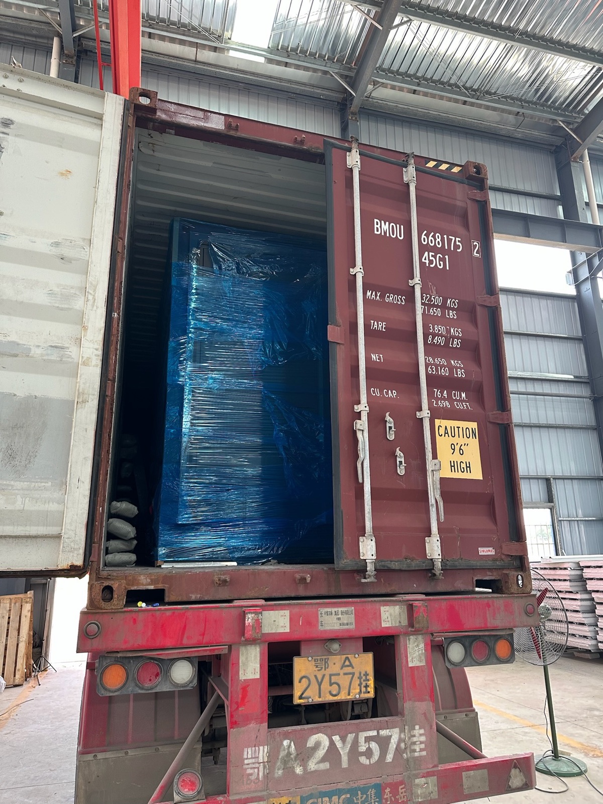 Open shipping container with a wrapped modular unit during factory loading