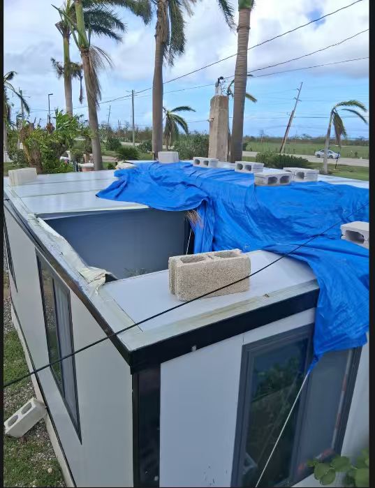 Post-storm roof-edge exposure on a small prefabricated building protected by a temporary tarp